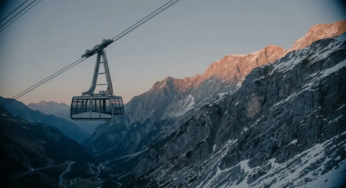 Moderne Seilbahn-Gondel steigt im Alpenglühen einen Steilhang hinauf